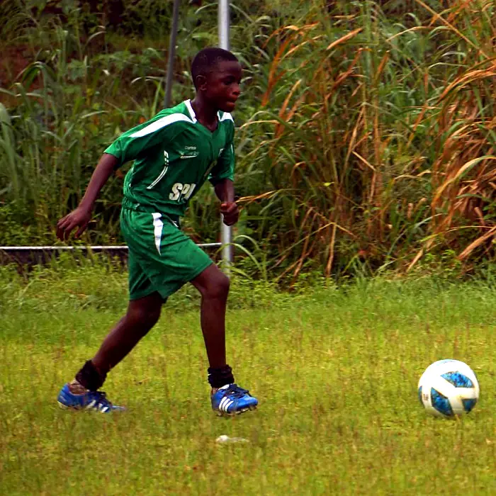 A young player in green dribbling the ball at a schools championship match