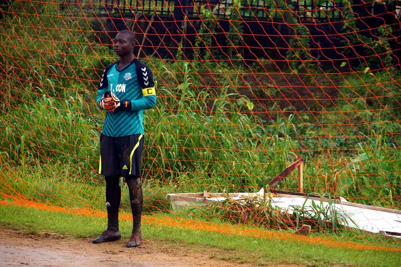 A goalkeeper in a teal shirt with a captain's armband standing in front of the net