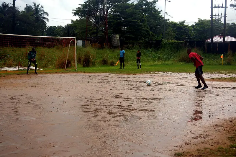 A player lines up a penalty on a waterlogged pitch while the goalkeeper waits