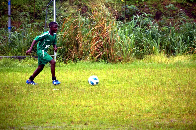 A young player in green dribbling the ball across the grass