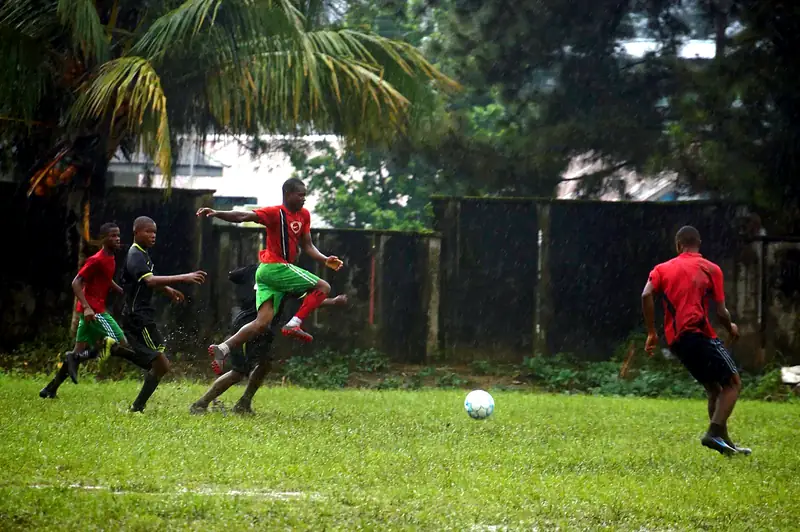 A player in red and green leaping over a challenge as rain falls on the pitch