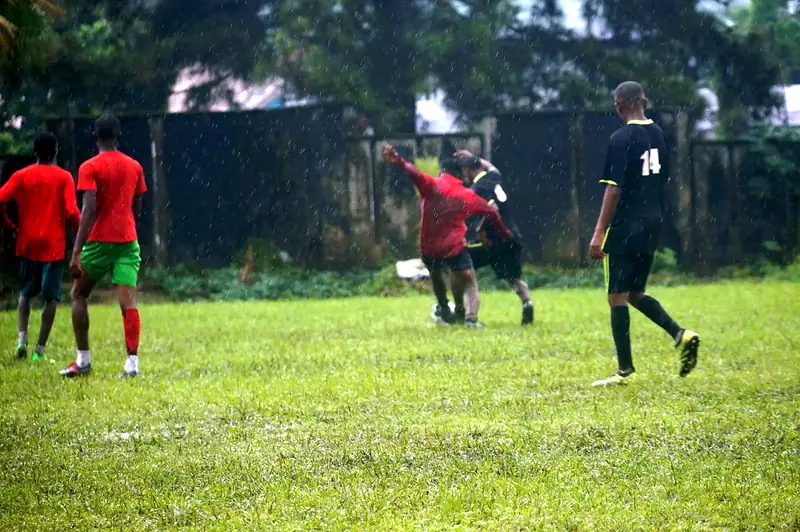 Two players tussle for the ball in heavy rain while teammates look on