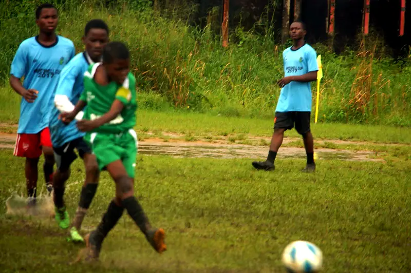 A player in green kicking the ball as water sprays off the wet pitch