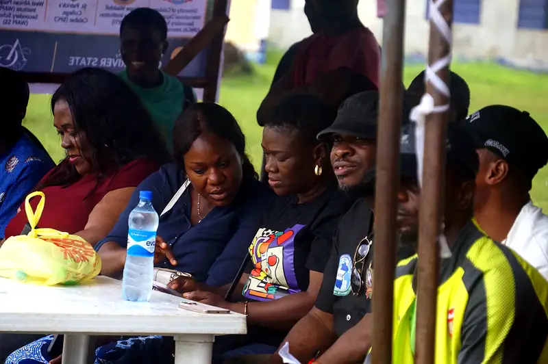 Officials and guests seated at a table under the tent, checking a phone together